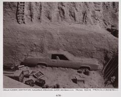 This photograph depicts a view looking down into an archeological dig site in which a buried car is being excavated.
