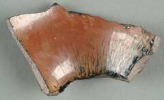 A curved, roughly-shaped five-sided shard with brown-black-russet glaze with hare's fur (兔毫盏 <em>tuhao zhan</em>) markings. Broken edges expose a gray ceramic body.