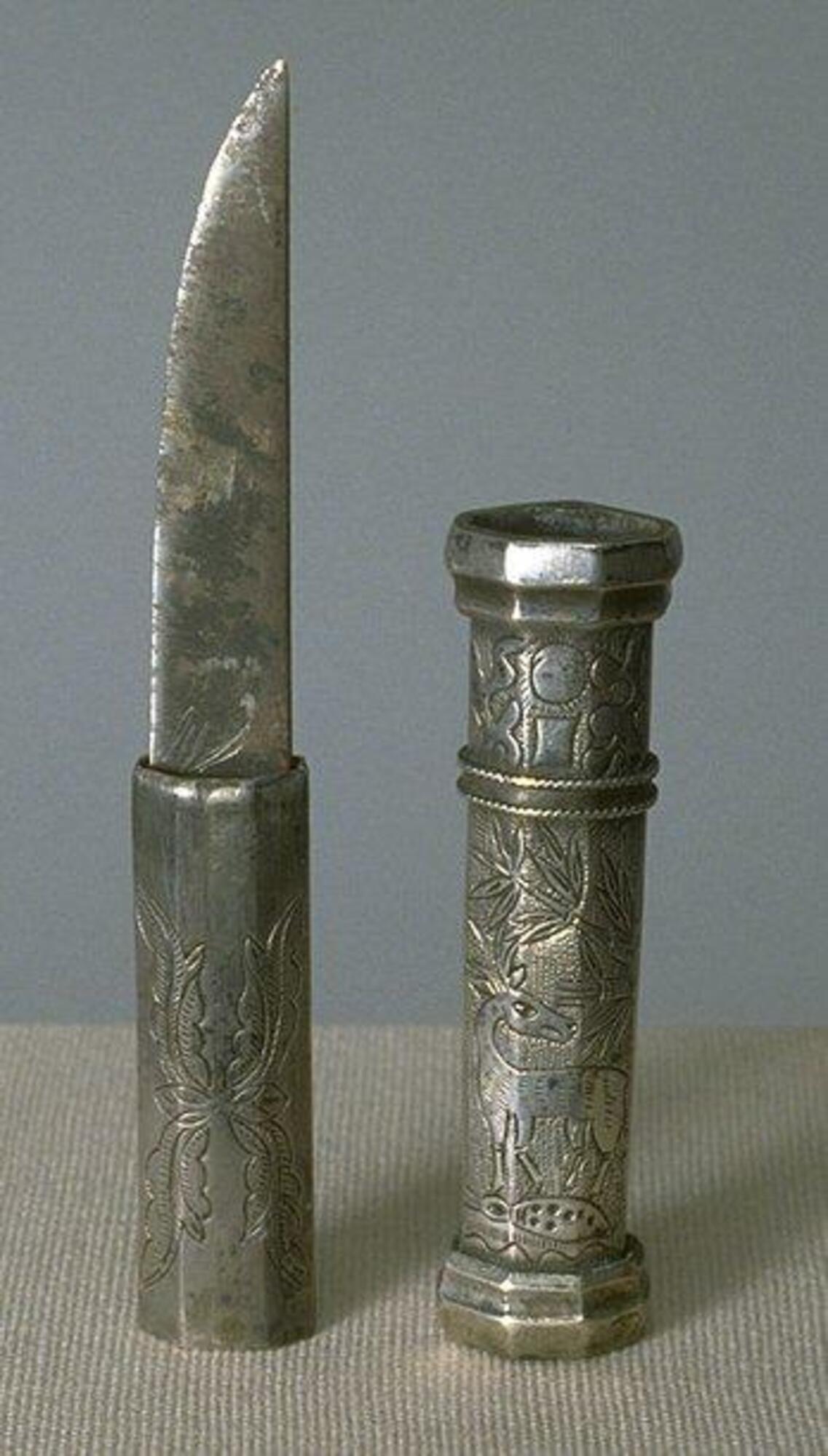 It is a knife made of silver. The sword blade was made of steel. Floral design was printed on the knob and Deer and bamboo was printed on the cover.<br />
<br />
This small knife is worn by a man. The handle and sheath are decorated with ten symbols of longevity against ring-punched background. The other side features engravings of plantains and lotus buds. Plantain symbolizes resuscitation from death and is one of the Eight Treasures of Taoism. The lotus flower symbolizes purity and the law of cause and effect as it emerges from mud (dirt) and bears seeds.
<p>[Korean Collection, University of Michigan Museum of Art (2017) p. 285]</p>
<br />
&nbsp;