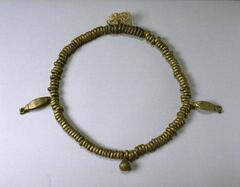 Belt with a band made of small brass rings and three pendants. One pendant is in the form of a crotal bell, while the other two pendants are in the shape of leaves. 