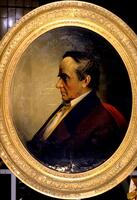 Portrait of a man in an oval frame, facing left. He has dark hair and is wearing a red coat and white shirt. Background is grey/brown.