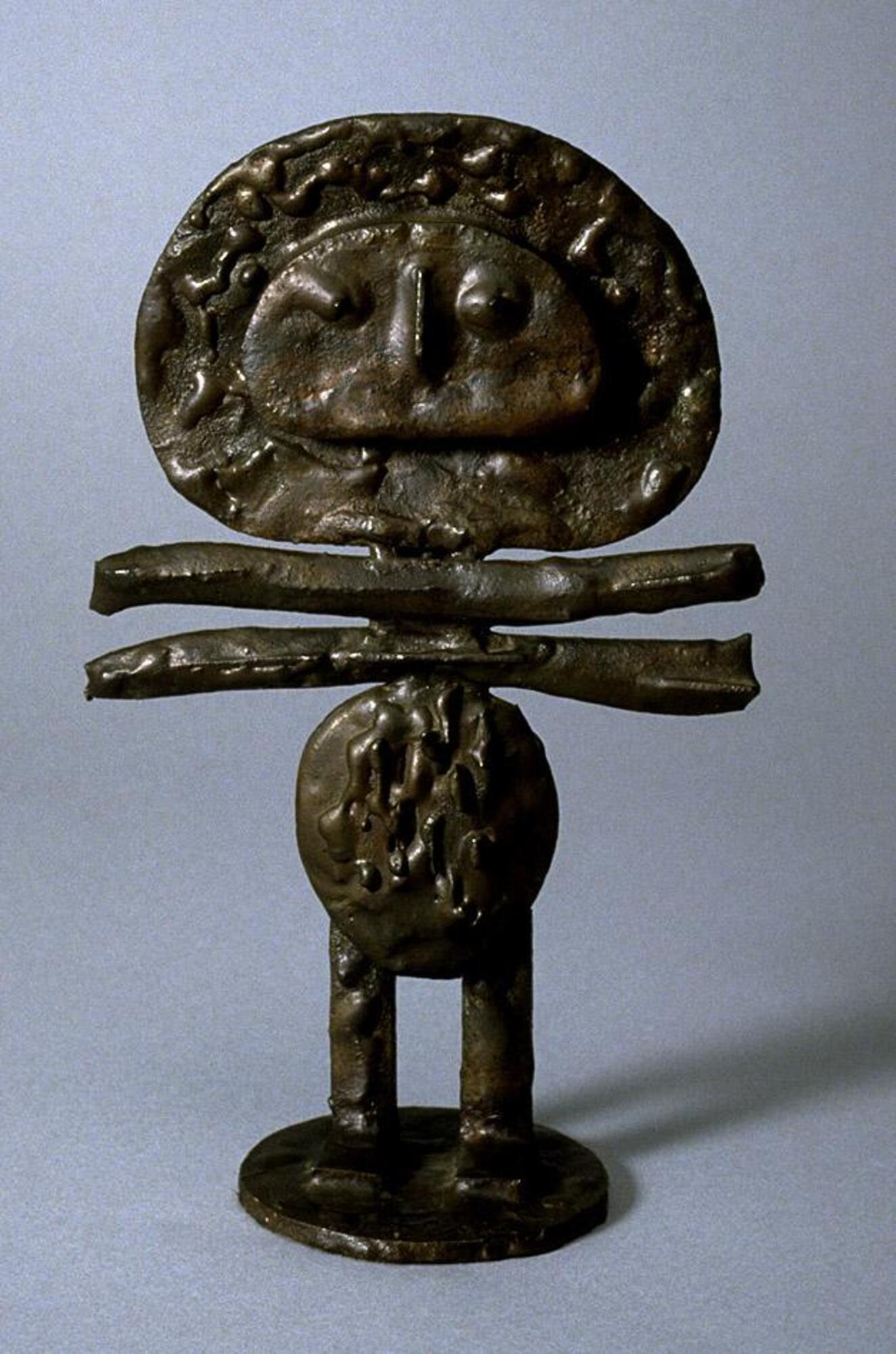 Highly abstracted figure with oval body, short straight legs, and a large mushroom shaped head with a crude, wide-mouthed face. Between the body and head are two horizontal bars that are slightly longer than the width of the head. The sculpture is quite flat, and the bronze has a molten look.