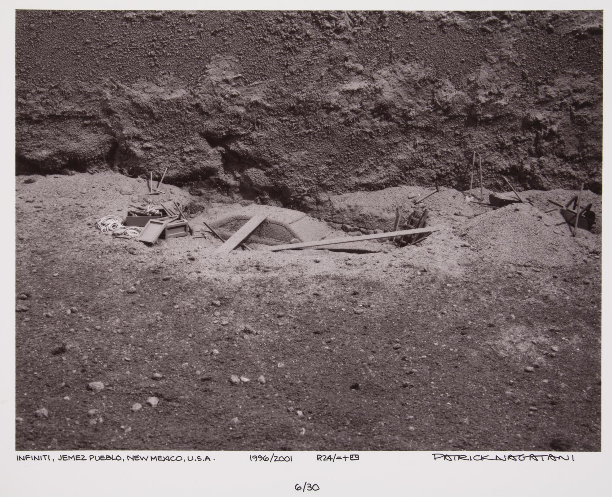 This photograph depicts a view looking downwards at an archeological excavation of a car.  There are shovels and other supplies strewn about the site.