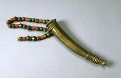 Brass horn with a string of brass and red beads attached to a cork stopper. The top edge and bottom edge of the horn are decorated with incised braided patterns. 
