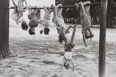 Girls hanging from a horizontal pole. One girl is doing a handstand on the ground and the girl hanging from the pole is holding her feet.
