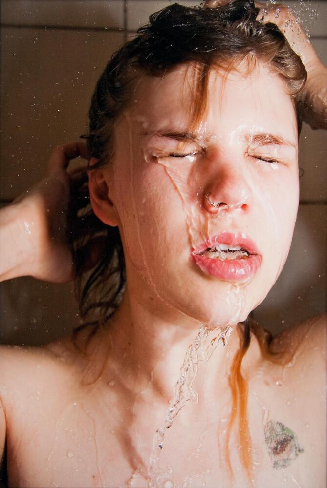 Head and shoulders of a girl in the shower, water streaming down her face.