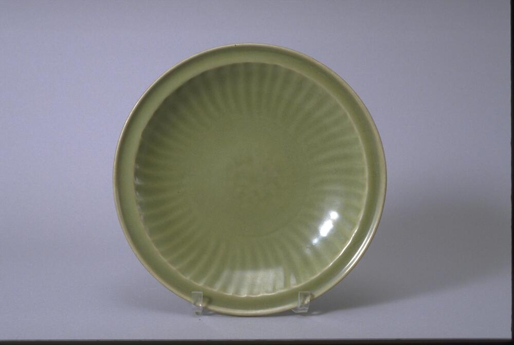 This is a wide, shallow stoneware bowl with everted rim, on a footring.  The interior is incised with a central peony motif surrounded by lotus petals, covered in a green celadon glaze. 