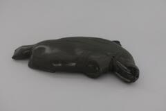A soapstone carving of a walrus lying on its stomach. There is a small wooden peg on the walrus&#39; stomach where it attaches to the base of Man Pulling Walrus.&nbsp;