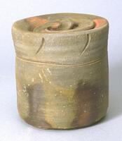 This is an unglazed stoneware bizen jar fired in a wood-burning kiln.<br />
It has a hard, smooth surface with decorative incisions near the top of the jar. The lower portion has effect of color gradation of reds and browns. The lid seems to dip into the jar, and has a know handle. The entire piece is not perfectly formed, but has an organic aesthetic.