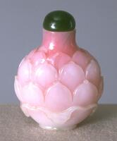A circular snuff bottle carved with ombr&eacute; pink lotus petals. On the top is a green stopper.