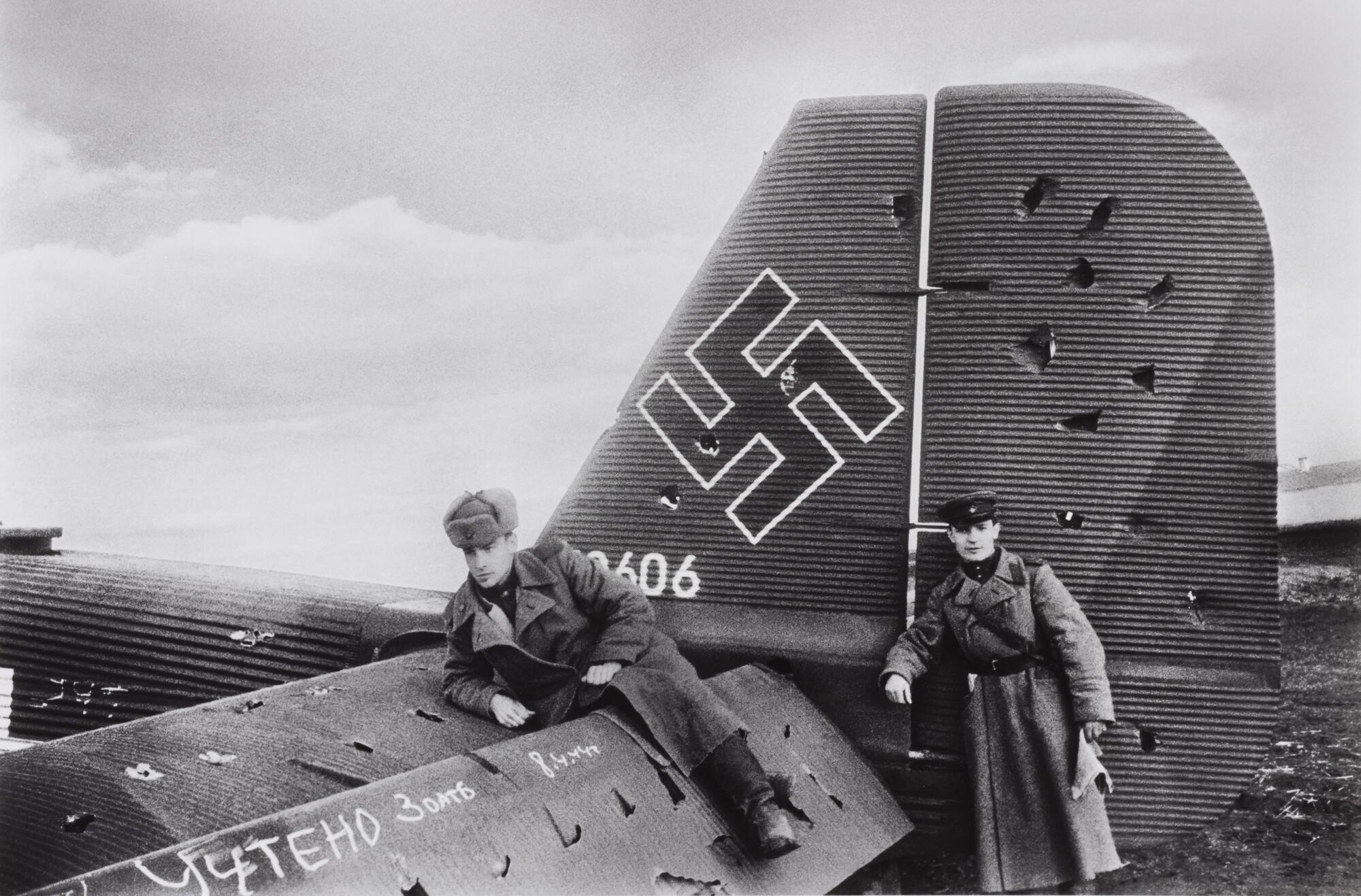 Two Soviet soldiers pose with a captured and heavily damaged Nazi warplane.