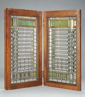 One of a pair of windows with a highly regular, rectilinear, although asymetric, design in both clear and colored glass. Window has an oak frame. Window design consists of vertical and horizontal bands of green and amber colorerd glass at top and bottom of window; along one side are colored squares of glass; along the other is a chevron-shaped column of glass. The overall effect is of colored pieces of glass suspended within a clear window subdivided by abstract bands and patterns of lead caming.