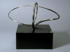 This is an abstract metallic sculpture with a black square base. The silver metal of the sculpture is little thicker than wire and forms two into intersecting circular shapes.