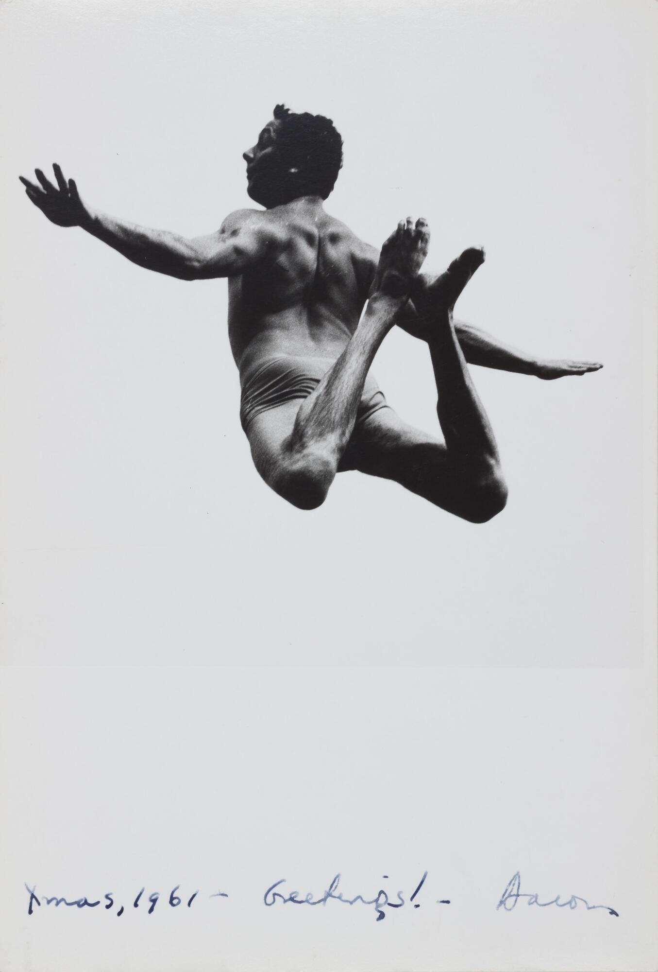 A photograph of a leaping man in mid-air with arms outstretched and legs tucked backward viewed from below.