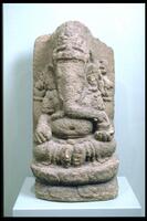 Ganesha is shown here seated on a double lotus throne, in a royal posture with the soles of his feet together. He has four arms, and holds two of his attributes in the rear pair: an ax and a rosary.  His trunk curls down across his rotund belly to reach for a bowl of sweets that rests in his left forward arm.  The cobra slung across his shoulder, now hard to make out because of the centuries of wear of the stone, indicates Ganesha's lineage as the son of the Shiva, in his aspect as the great ascetic. Almost 27 inches high, this sculpture of the Hindu god Ganesha is carved of andesite, a volcanic stone common to the island of Java in Indonesia. Andesite is a soft stone and erodes easily, which is why the carving is no longer crisp.