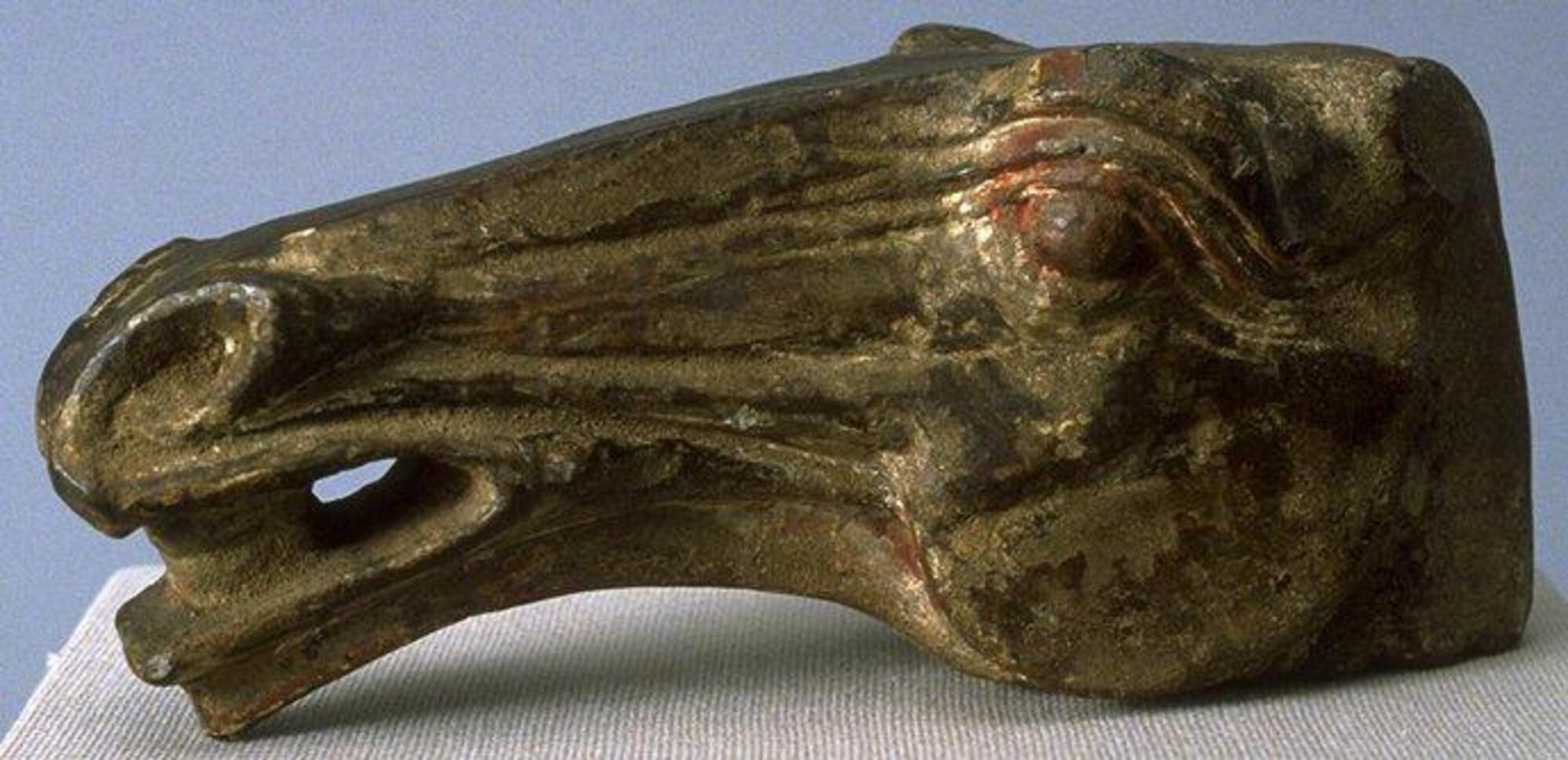 A gray earthenware head from a horse sculpture vividly sculpted to show the musculature of the horse's face with flaring nostrils and an open mouth showing its tongue. It has deep set and bulging eyes and loss of ears and neck. The head has traces of red and white mineral pigment. 