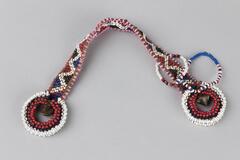 Beaded bracelet with triangle design. Pink, white, blue, red, and black beads on brown thread. Bracelet ends have large round beaded area. Two small beaded loops attached. White tag attached.