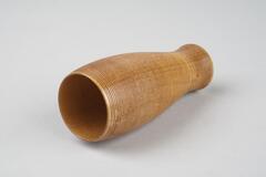 Wooden vase-like shape that is ribbed. Light wood in color.