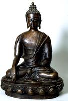 A hollow cast bronze sculpture of the Buddha, including a lotus base. The bronze has a dark, shiny patina over most of its surface. <br />The Buddha sits with his legs crossed in the padmasana pose; his right hand reaches down, palm inwards, to touch the earth, in an elegant gesture with just the tip of his third finger making contact, while his right hand rests in his lap. His torso is tall and erect. His dhoti (a skirt-like garment) is tied high on his torso, while his outer robe covers his left shoulder completely and just brushes against his right shoulder. His face is shaped like a tall and narrow "U," with wide, gently arching brows, downcast eyes under swelling lids, a long and high nose, and full, cupid's-bow lips. The urna, an auspicious mark on his forehead, is indicated here by a small bump with an incised outline. His hair is arranged in rows of snail-shell curls, which are repeated in a larger size on his ushnisha, culminating in a lotus bud.<br />The upward-pointing lotus petals on the dais are 
