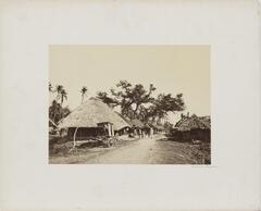 View of a village with a dirt road lined with thatched-roof structures.