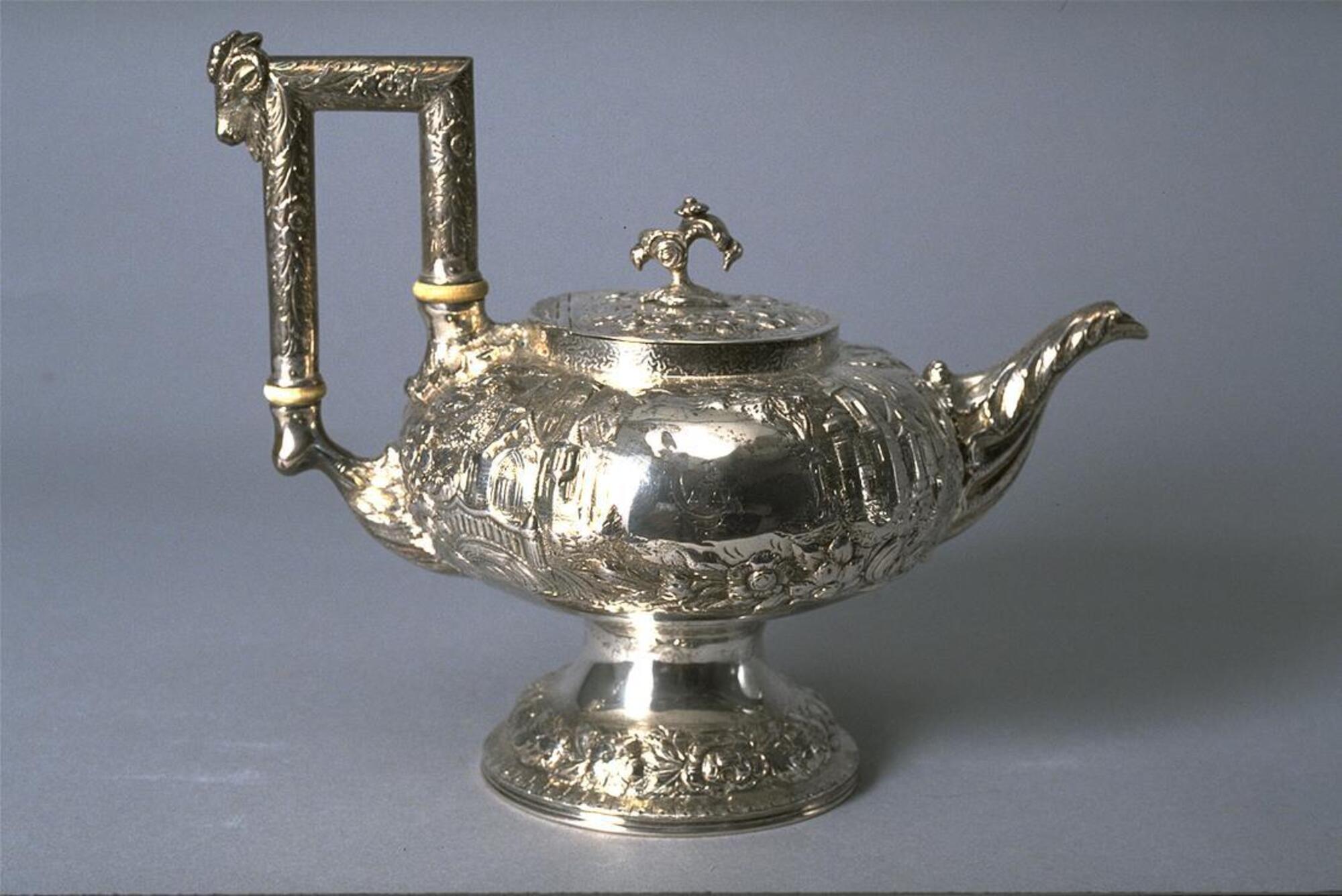Short, squat silver pot with short spout, finial-topped lid, tall square handle and opulent repouss&eacute; decoration