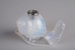 A clouded glass inkwell in the shape of a snail.  The inkwell has a metal insert in the shell of the snail, but no lid.