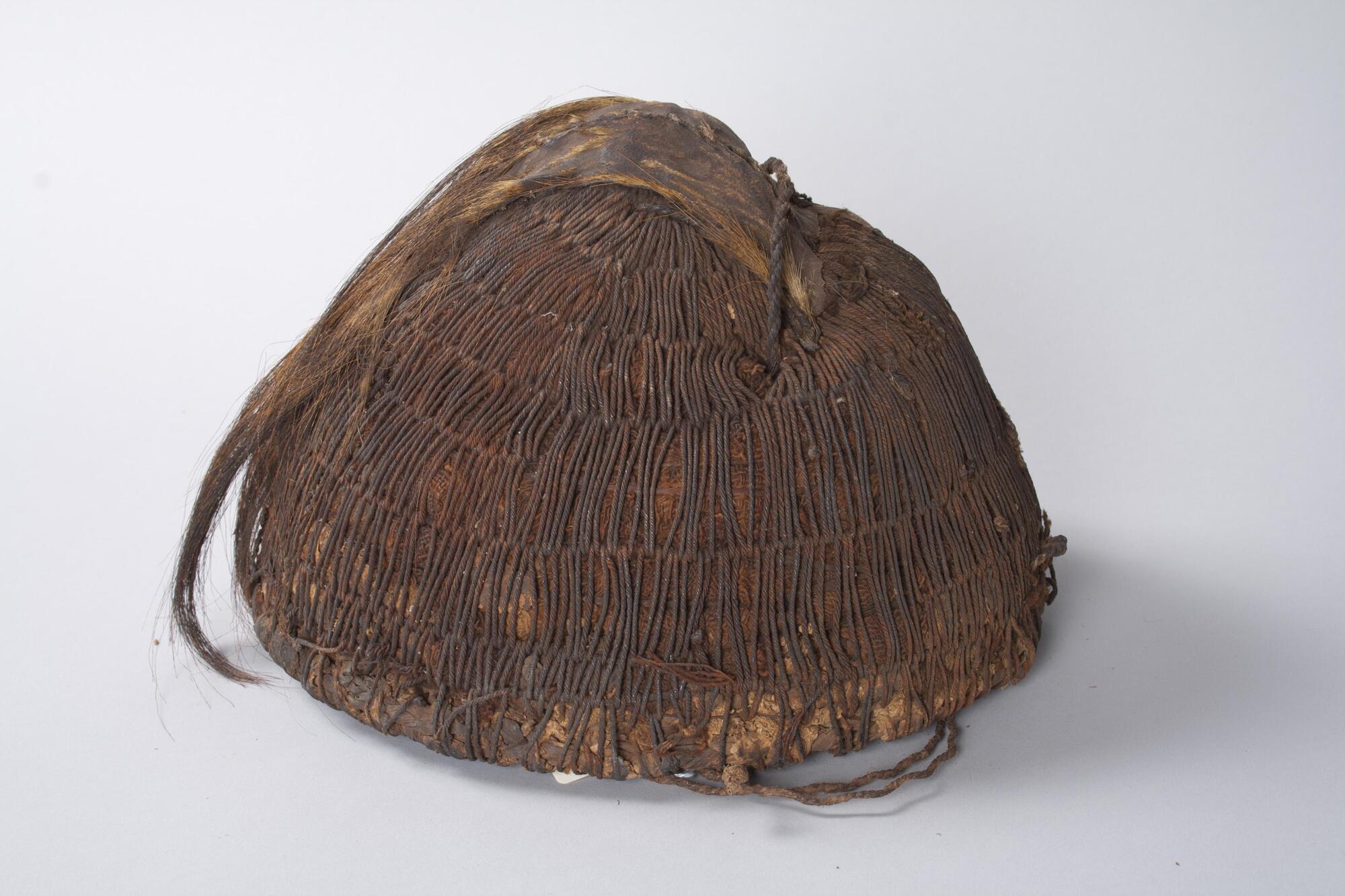 Cap in a dome shape made from woven fibers with a piece of fur attached to the top, possibly from a monkey. 