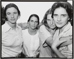 Group portrait of four women standing outdoors. The right two are locked in an embrace.
