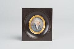 Portrait of a white-haired man with glasses wearing a high-collared white shirt and gray coat. The image is mounted in a round gold frame within a black wooden frame.