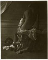 A photograph of a nude man sitting on a bed, his back turned toward the viewer. Cloth drapes over the end of the bed, curtains drape over the walls, and a battle helmet sits at his feet. 