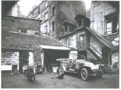 Courtyard behind a group of buildings with a car and several motorcycles parked in front.