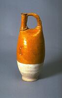 This is a stoneware flask with amber glaze on the upper portion. The lower portion is unglazed, showing white slip.