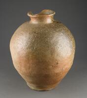 A large storage jar with round shoulder and shorter neck. The body is rather unevenly potted, showing bumps in some parts. The surface texture is uneven with speckles of white particles. Dark green, natural ash glaze drips on one side of the jar from top of the neck to the lower middle of the body. The rim of the neck is partially chipped and cracked. It has no foot.