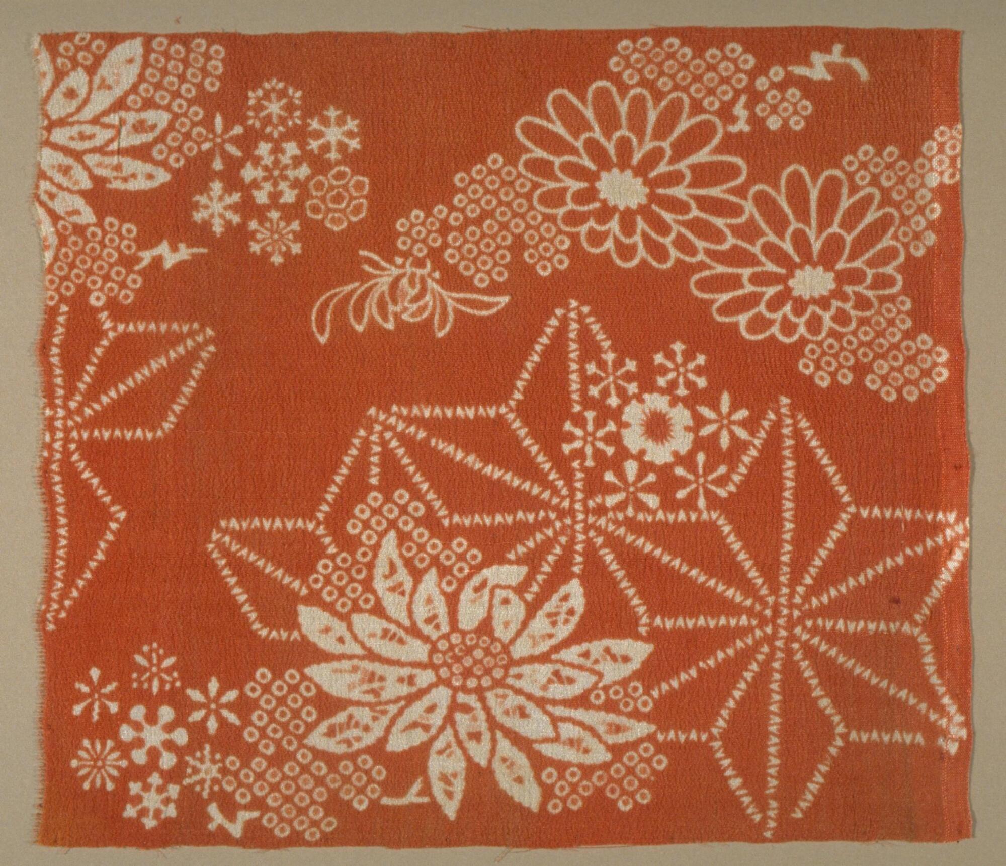 A red kimono fragment, with white stenciled design of chrysanthemums, hemp-leaf flowers, and snowflakes.