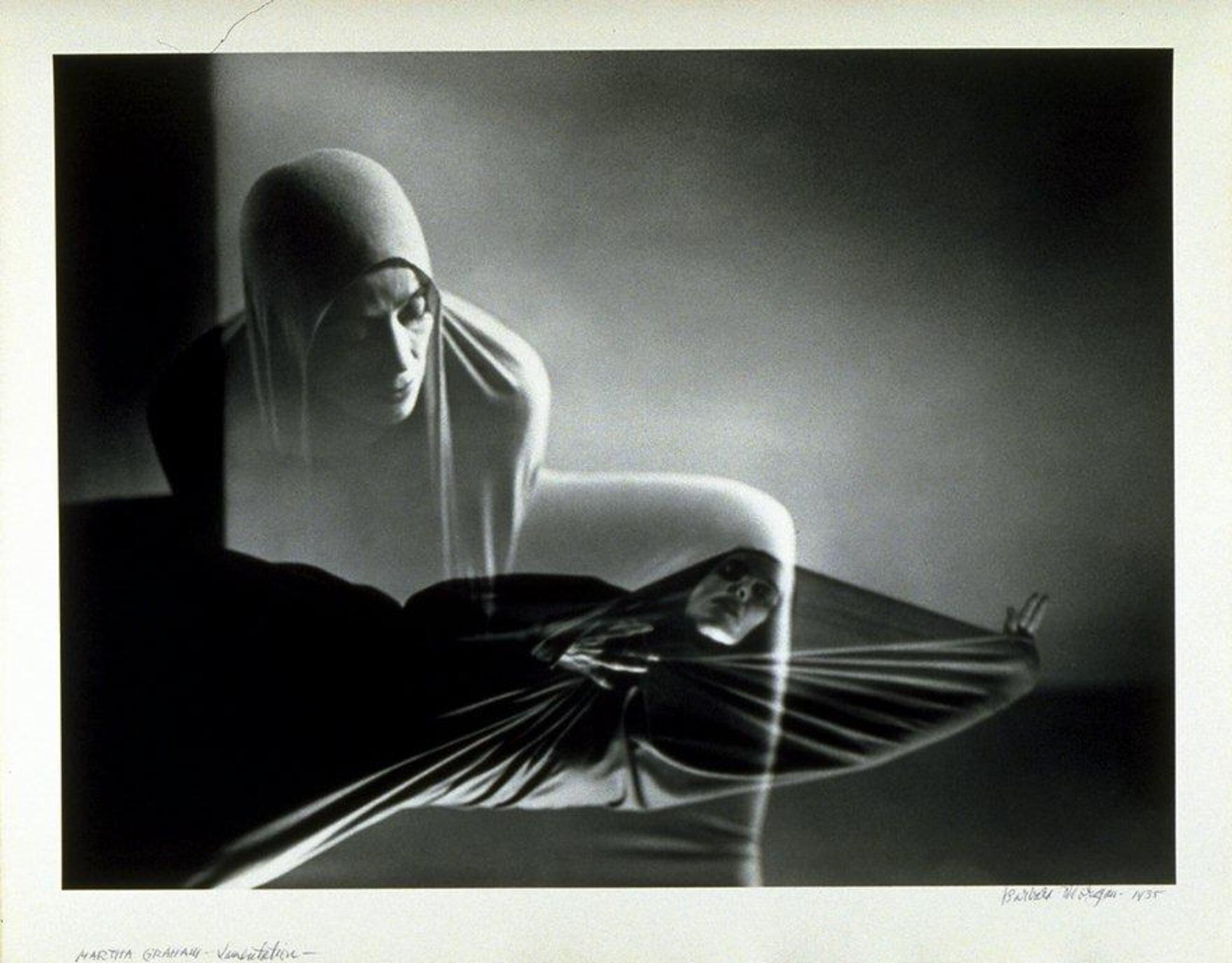 A composite print from two negatives, each representing a moment from a dance performance. The woman wears a large cloth, which she manipulates with her motions to create forms and shapes.