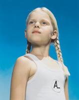 A blonde girl with braids looking to the left in front of a blue background.
