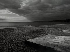 A black and white photo of a beach. The words "shore" appears over the water, while "coast" appears on the sand.