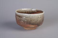 Tea bowl with natural ash glaze, which creates gray, black, white, and orage tones on the piece, speckled with black.