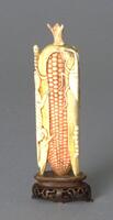 A yellow ivory snuff bottle in the shape of corn. There are nibbles carved on the surface of the snuff bottle and husk surrounding it. The stopper is shaped like a stem. The snuff bottle is sitting on and incised wooden stand.
