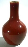 Vase with globular body tapering to the foot and to a tall, straight neck, covered in a thick, deep blood-red glaze that thins at the lip exposing the color of the white porcelain clay body below.