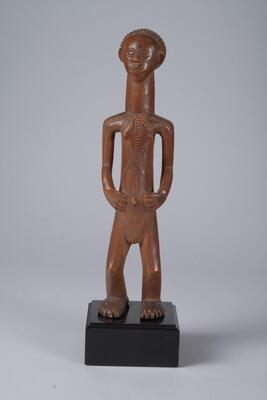 Carved wooden figure of a human. The torso, neck and head make an elongated cylinder along the certical axis. The hands rest at its sides near the umbilicus. The hair, face, hands, genitals, and feet are detailed.