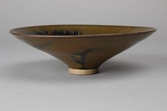 A conical, wide-flaring buff stoneware teabowl with a direct rim on a straight footring, covered with black glaze with russet brown mottling on the exterior and russet streaks on the interior. 