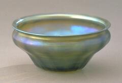 Glass bowl-shaped vessel with the suggestion of lobes with a large flared lip and iridescent in color in shades of greens and blues
