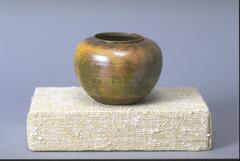 Round-bodied vessel with small lip and wide mouth covered in an iridescent glaze over a semi-matte glaze that creates an appearance of irregular patches of color in browns and olive greens