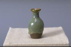 This small vase has a thick blue-green glaze that extends down about 3/4 of the vessel; the base remains unglazed, exposing the brownish clay body.