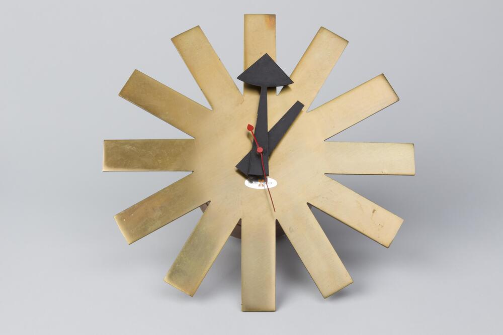 Wall clock in the shape of a cut out asterisk, with wide black hour/minute hands and red second hand.