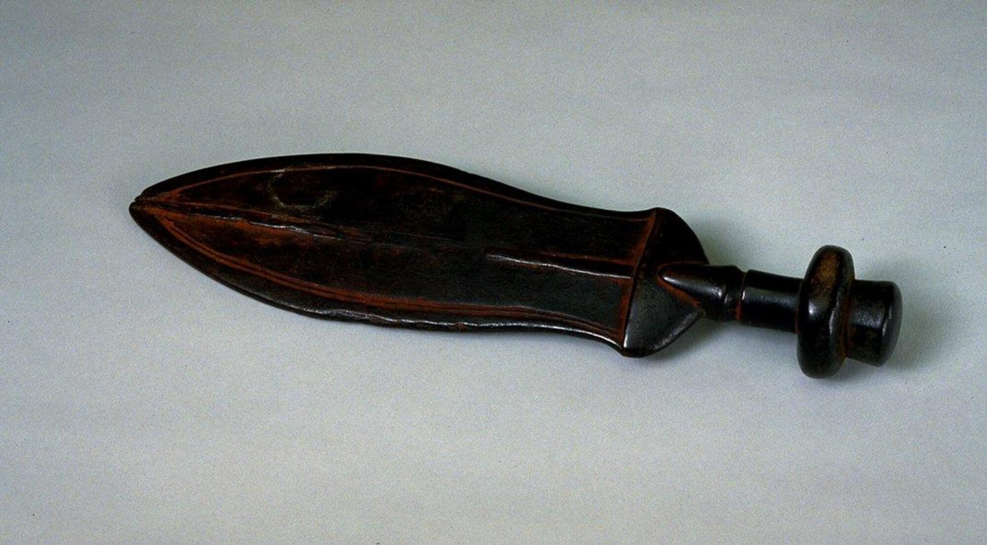 Wooden knife with a leaf shaped blade. The center of the blade has a carved line running down the length of the blade. The knife has patination. There is tukula powder rubbed on the knife. 