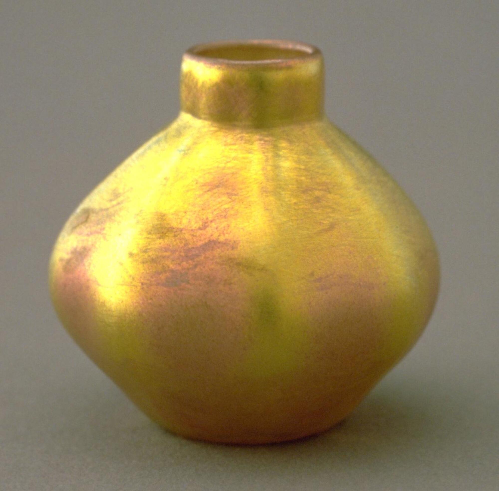 Miniature vase of irregular, slightly globular form; vessel has suggestions of lobes and has a narrow neck. Exterior of vase exhibits a deep yellow and pinkish iridescent surface with an overall effect of rich color and natural aysmmetry.