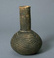 Terracotta bottle with a bulbous belly and a long cylindrical neck. Black ash firing finish on entire bottle with ethched geometric design on belly.