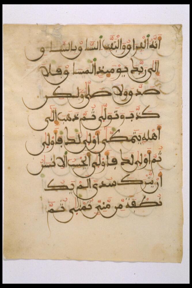 Arabic calligraphic script on paper; script is in Maghribi style, written in black ink with touches of green and rec ochre. Shadows of script (from reverse or opposite page, transferred while closed?) show through. Beige paper is browned with age at edges; upper left has repaired tear.